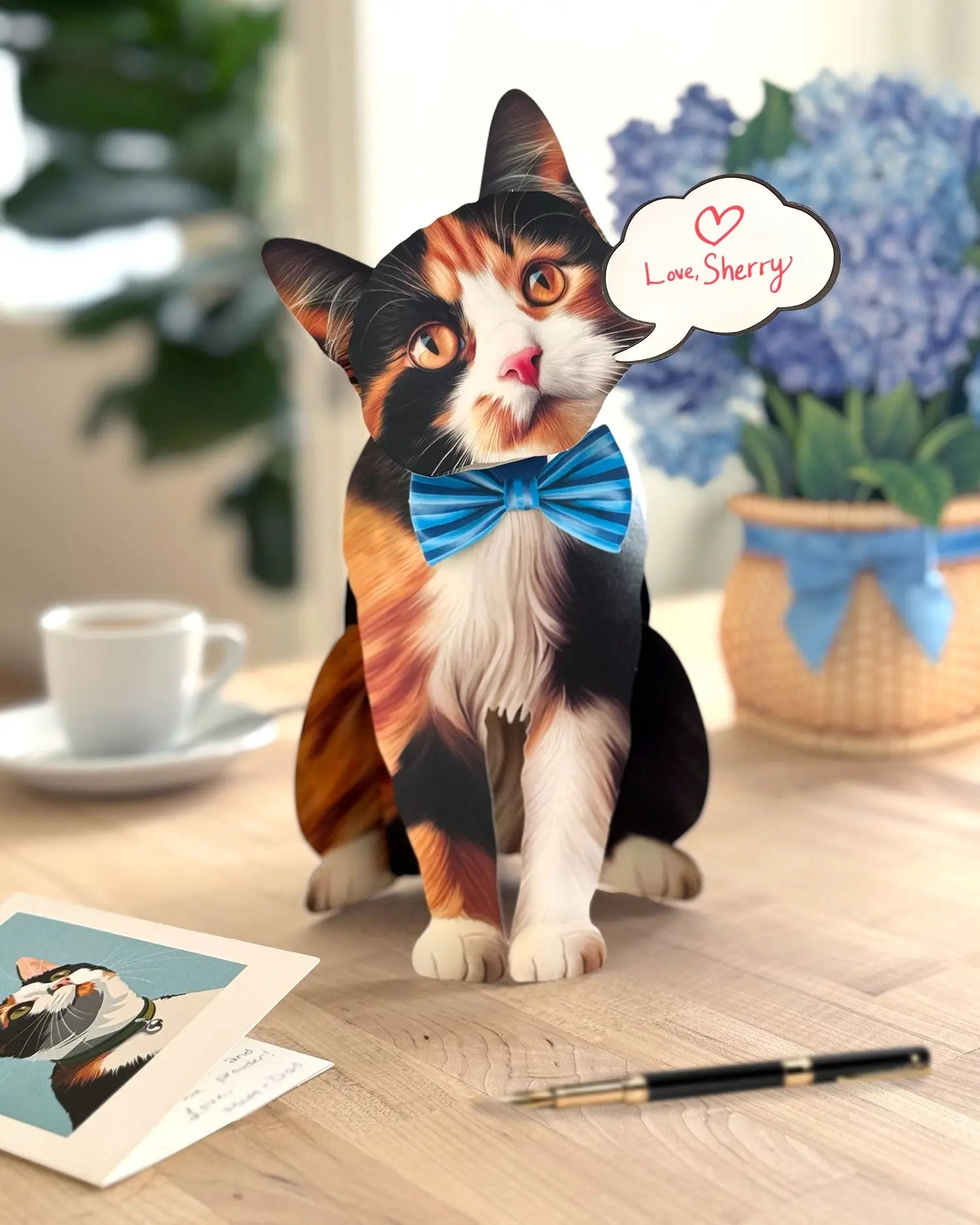 FreshCut paper calico cat pop-up card on a desk with a cup and flowers in the background.