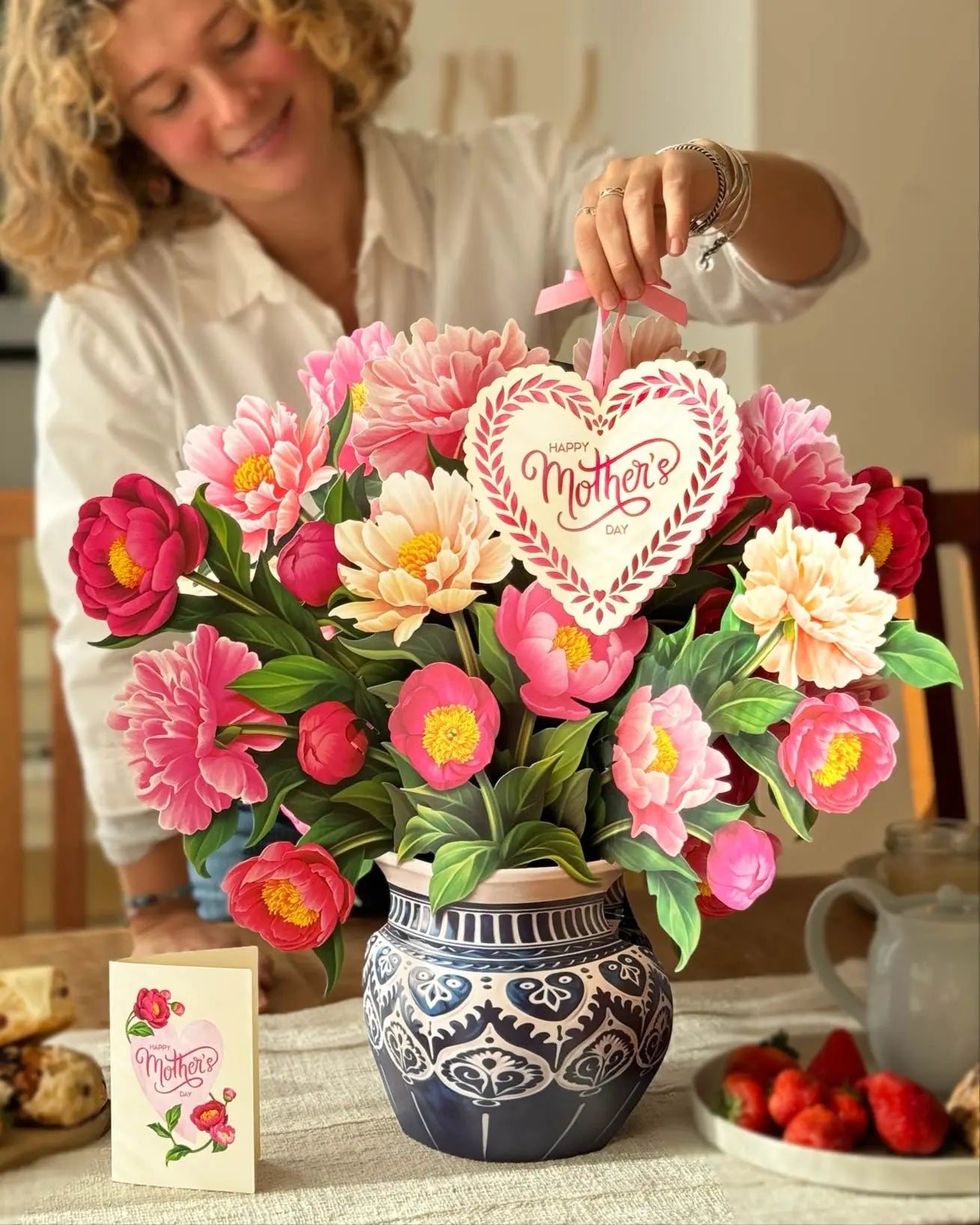 a woman holding a heart shaped cookie in a vase of flowers