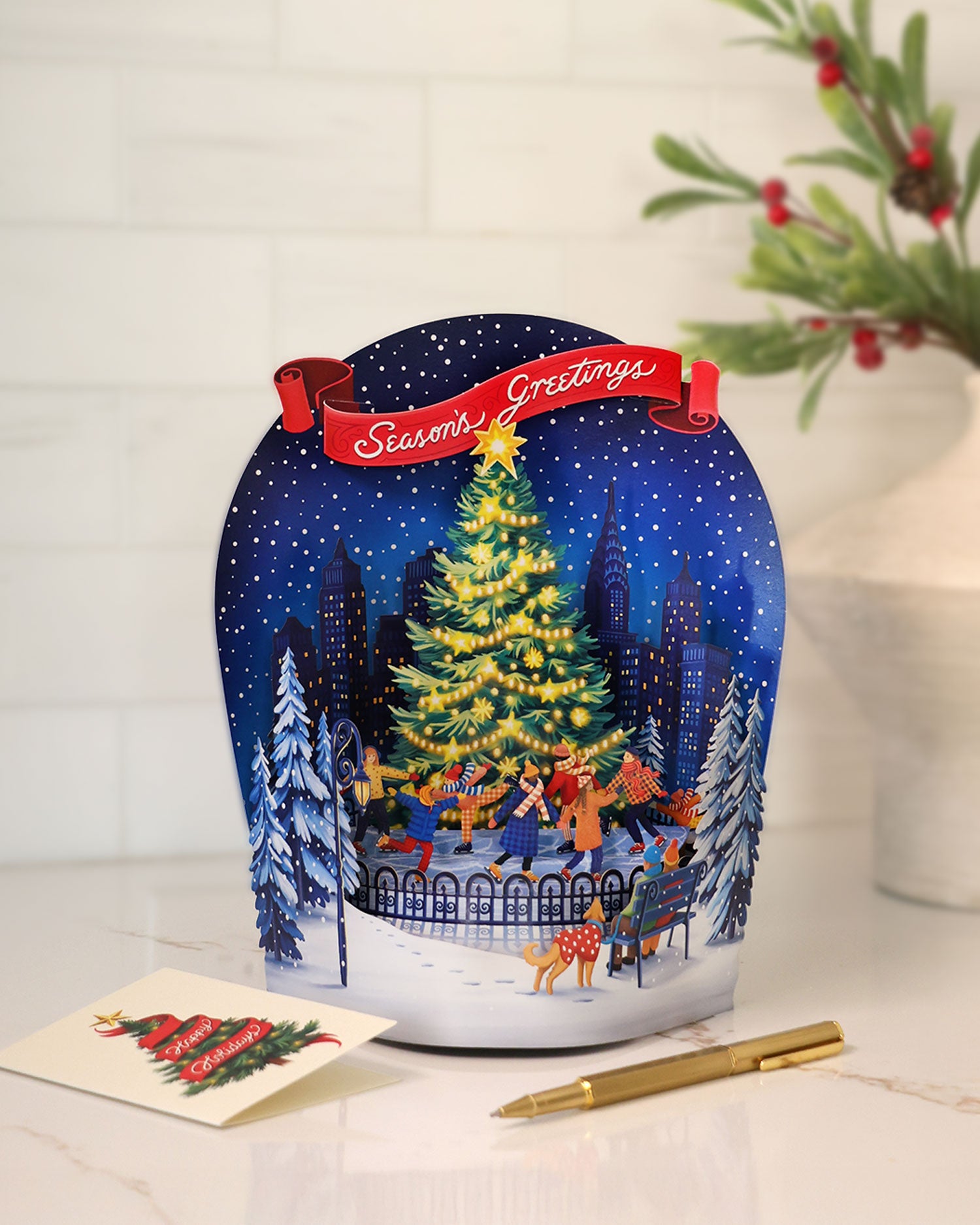 Decorative Christmas card with a snowy scene and animated figures, featuring a pen and card on a white surface.