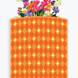 A Halloween-themed branded envelope bag packaging with an orange and yellow argyle pattern featuring small ghost motifs, with a colorful floral pop-up peeking out and a purple banner reading 'Happy Halloween!'.