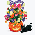 A colorful Halloween illustration featuring a carved orange pumpkin filled with bright multicolored flowers, a purple 'Happy Halloween!' banner, small ghost decorations, and a paper black cat lying beside it on a light gray background.