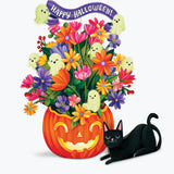 A colorful Halloween illustration featuring a carved orange pumpkin filled with bright multicolored flowers, a purple 'Happy Halloween!' banner, small ghost decorations, and a paper black cat lying beside it on a light gray background.