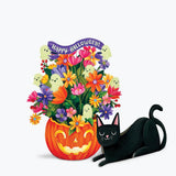 A festive Halloween illustration featuring a carved orange pumpkin filled with colorful flowers, small ghost figures, and a purple 'Happy Halloween!' banner, next to a paper black cat on a light gray background.