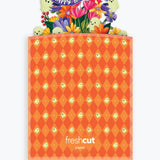 An orange Halloween-themed branded envelope with a diamond pattern and a colorful pop-up 'Happy Halloween!' floral and ghost design at the top, shown on a light gray background.