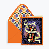 A Halloween greeting card and matching envelope on a light gray background. The card features a purple night sky with a haunted house, bats, a cat, and a cream banner reading 'Happy Halloween!'.
