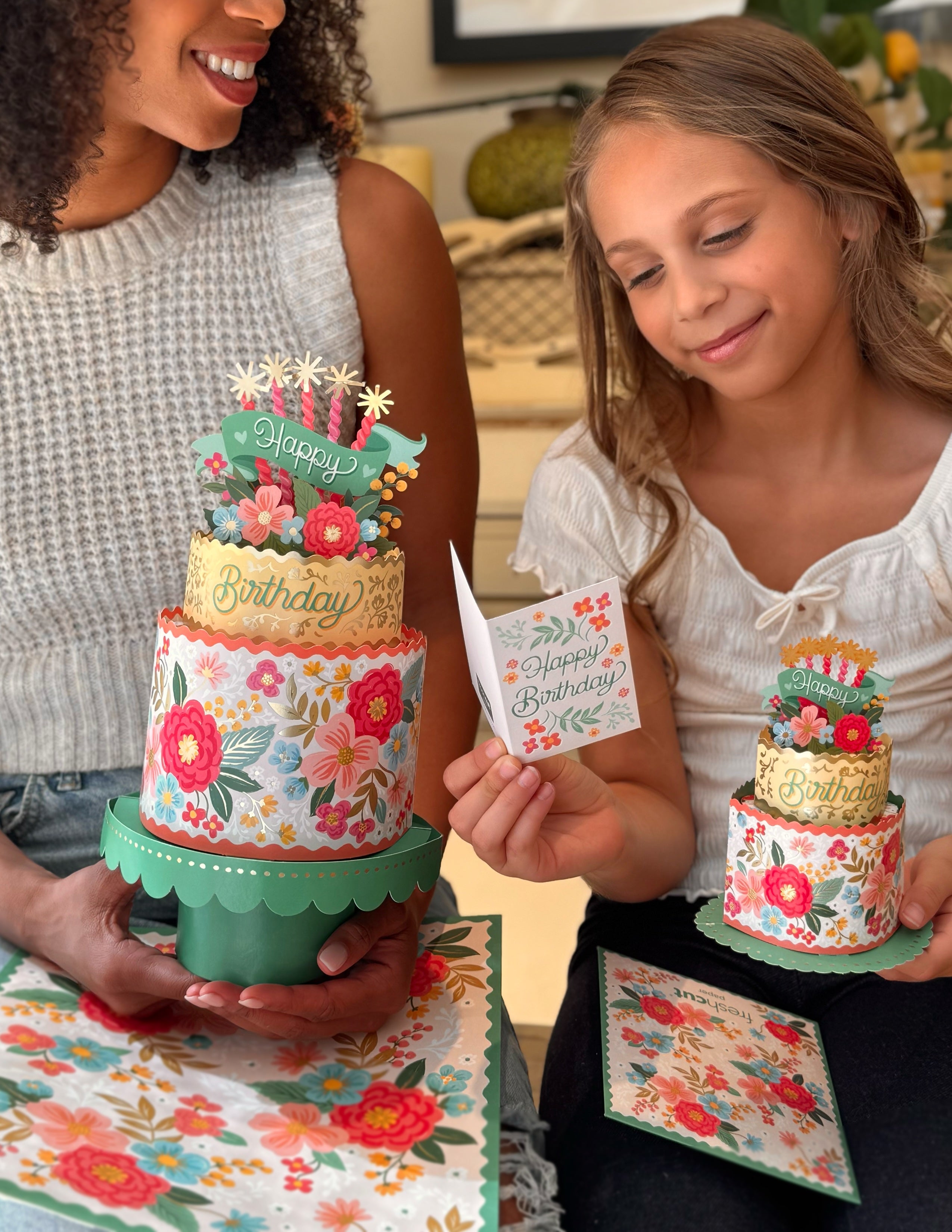 Two people holding small floral birthday cakes with decorative cards.
