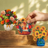 Three decorative paper flower arrangements displayed on rustic wooden steps against a beige wall with leaf shadows. A human hand is reaching toward the center arrangement, which is a small autumn-themed basket with pumpkins, sunflowers, and berries.