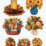 A set of autumn-themed decorative illustrations on a white background, including a glowing pillar candle in a floral base, sunflower bouquets in blue and white vases, a fall harvest basket with pumpkins, grapes, and wheat, and smaller floral arrangements. A small orange circle at bottom left reads '2X EACH'.