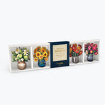 A boxed floral magnet set displayed against a light gray background. The package contains four decorative magnets shaped like vases with flowers, including white lilies, yellow sunflowers, red roses, and pink peonies, with a dark blue center label reading 'Mini Bloom Magnets'.