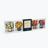 A boxed floral magnet set displayed against a light gray background. The package contains four decorative magnets shaped like vases with flowers, including white lilies, yellow sunflowers, red roses, and pink peonies, with a dark blue center label reading 'Mini Bloom Magnets'.