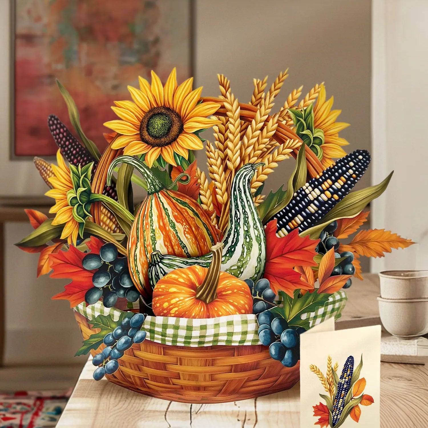 Golden Harvest pop-up bouquet featuring sunflowers, pumpkins, gourds, colorful Indian corn, wheat stalks, autumn leaves, and blue berries arranged in a woven basket beside a matching greeting card.