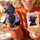 A woman in an orange sweater holds a black cat pop-up card dressed as a witch in a purple hat and cape with a broom, alongside a small 'Happy Halloween' card and a printed photo of the cat.