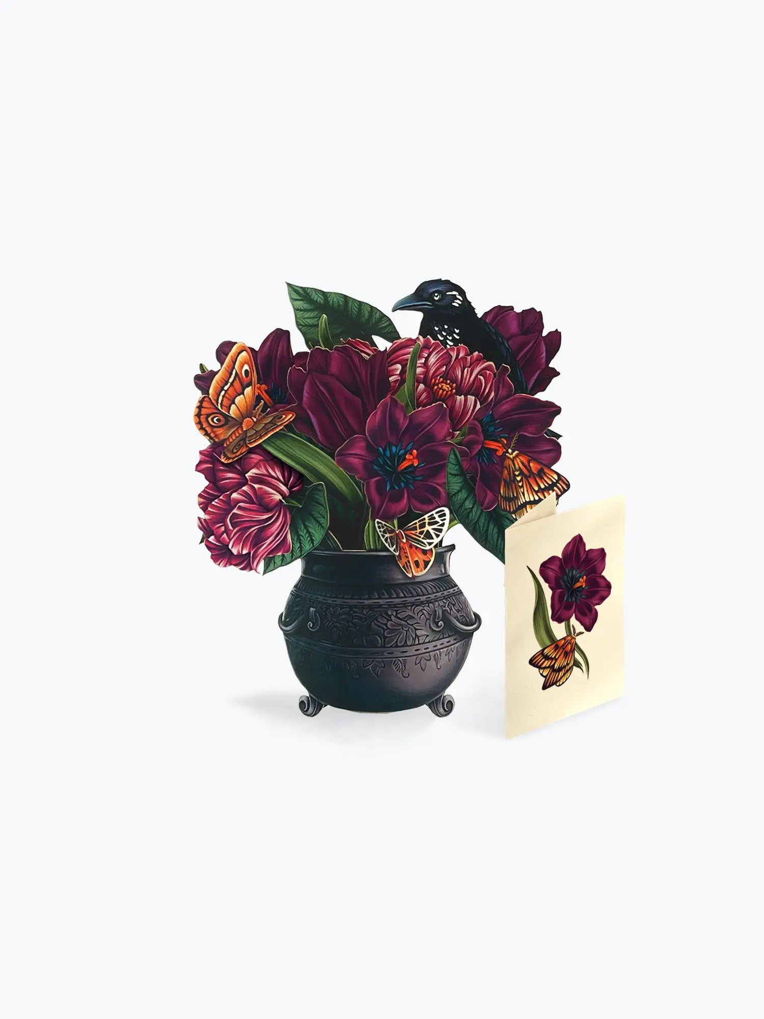 A decorative illustration of a black cauldron filled with dark purple flowers, green leaves, orange butterflies, and a black bird, shown beside a small cream card with a matching floral design on a light gray background.