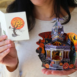 Person holding a pop-up card with a haunted house design